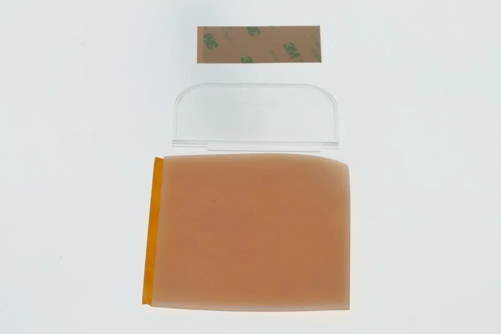 Transparente Isolierplatte von Bosch liegt flach auf einer weißen Oberfläche, daneben ein kleines Stück Klebeband. Die Platte hat abgerundete Ecken und eine orangefarbene Unterseite.
